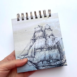 Peut inclure: Un petit bloc-notes à spirale avec une illustration en noir et blanc d'un voilier sur un fond bleu clair et beige. Le bloc-notes a un thème nautique vintage.