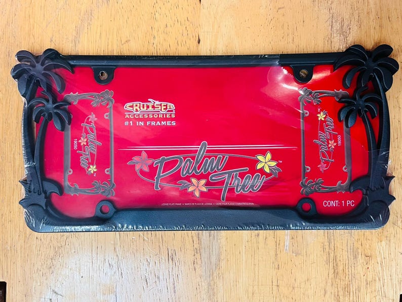 May include: Black license plate frame with a red background. The frame features palm tree cutouts at each corner and the words "Palm Tree" in a stylized font. The text "Cruiser Accessories #1 in Frames" is also visible.