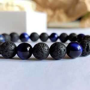 Puede incluir: Un brazalete hecho de cuentas de lava negra y ojo de tigre azul.