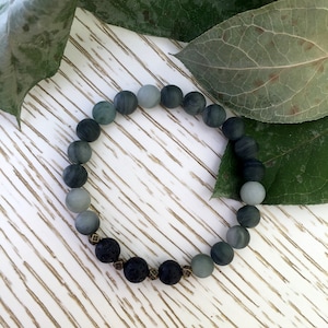 May include: A grey and black beaded bracelet with a mix of round and faceted beads. The bracelet is made with lava rock and agate beads.