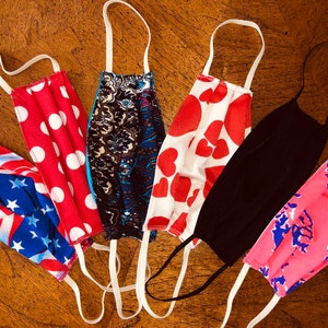 May include: Six different fabric face masks with various patterns. The masks are all made of cotton and have elastic ear loops. The patterns include polka dots, hearts, stars and stripes, paisley, and abstract designs.