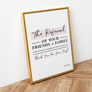May include: A gold framed print with a white background and pink text that reads "The Referral of Your Friends + Family Is The Greatest Compliment You Can Give Us Thank You For Your Trust".