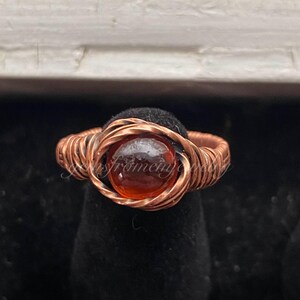 May include: A copper wire wrapped ring with an orange gemstone in the center.