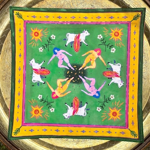 May include: Square green scarf with a colorful illustration. The design features white cows with orange wings, nude figures with colorful hair, suns, and flowers. The scarf has a yellow and pink border.
