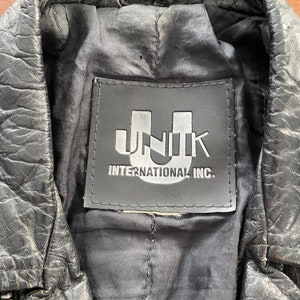 May include: Close-up of a black leather jacket with a black label that reads "UNIK INTERNATIONAL INC."