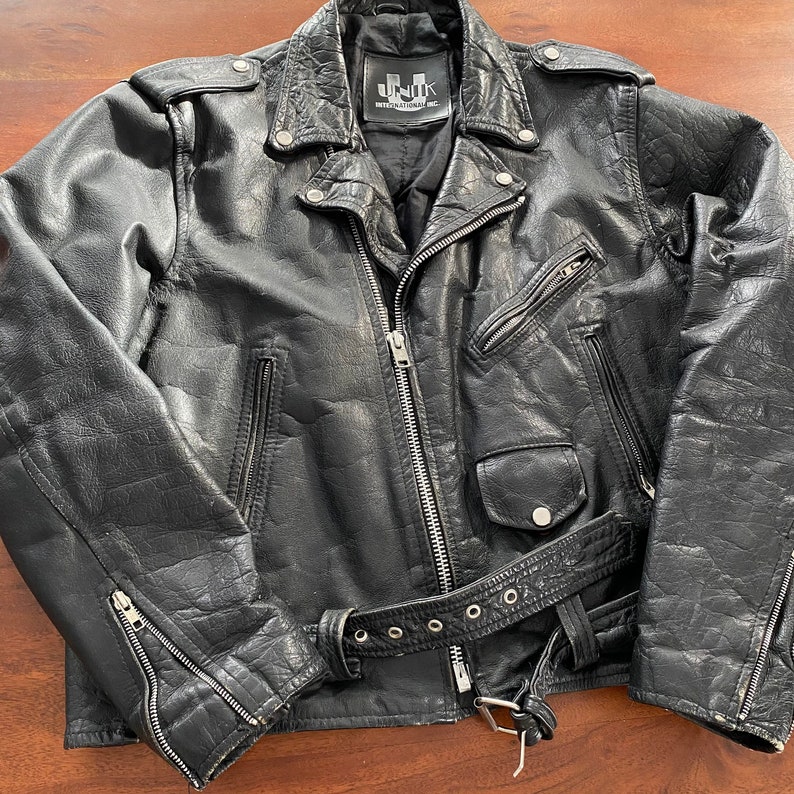 May include: Black leather motorcycle jacket with a zip fastening, a belt, and a UNIK INTERNATIONAL label.