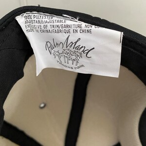 K&ouml;nnte beinhalten: Ein wei&szlig;es Etikett mit schwarzem Text, auf dem steht: "100% Polyester, Verstellbar/Einstellbar, Exklusiv f&uuml;r Besatz/Verzierung Nicht-Cop, Hergestellt in China/Fabriqu&eacute; en Chine, Palm Island Trading Corp."