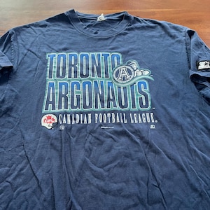 May include: Navy blue Toronto Argonauts t-shirt. The shirt features the team name and logo in teal and white, with the Canadian Football League logo below. The Starter logo is visible on the sleeve.