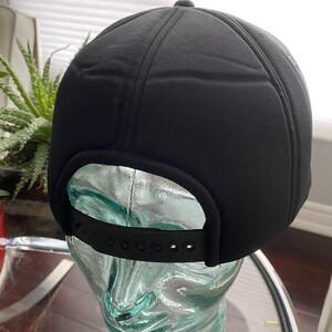 K&ouml;nnte beinhalten: Schwarze Baseballkappe mit schwarzem verstellbarem Riemen. Die Kappe ist aus weichem, gestepptem Material.