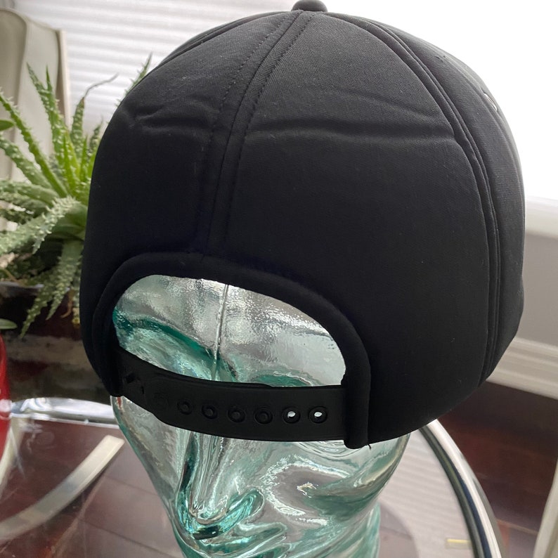 K&ouml;nnte beinhalten: Schwarze Baseballkappe mit schwarzem verstellbarem Riemen. Die Kappe ist aus weichem, gestepptem Material.