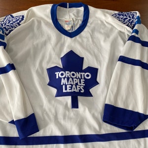 May include: White hockey jersey with blue and white stripes. The jersey has a blue maple leaf with "Toronto Maple Leafs" written on it.