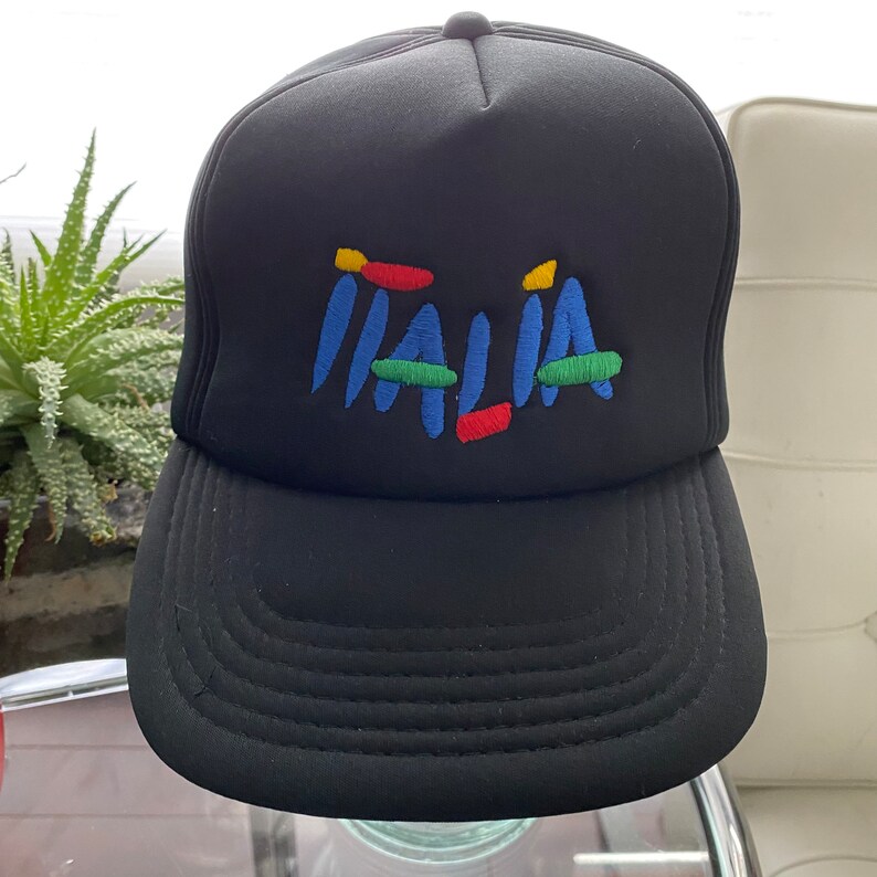 K&ouml;nnte beinhalten: Schwarze Trucker-Kappe mit einem bunten gestickten "ITALIA"-Logo.