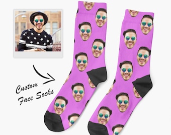 May include: A pair of bright purple socks featuring a repeating pattern of a smiling person wearing round blue-tinted sunglasses. The socks have black heels and toes. A small inset photo shows the person, with the text Custom Face Socks.