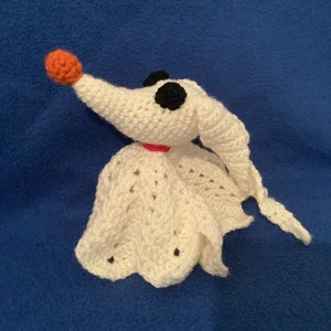 May include: White crocheted amigurumi toy resembling a dog with a red nose, black eyes, and a white crocheted cape.