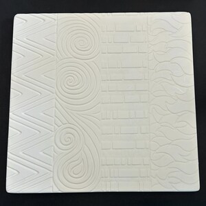 May include: A square, off-white ceramic tile with four distinct textured patterns. The patterns include a zig-zag, a spiral, a brick-like design, and a wavy pattern. The tile is set against a black background.