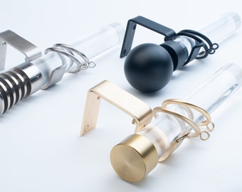 May include: Three curtain rods with different finials. The first is silver with a ribbed finial, the second is black with a round finial, and the third is gold with a round finial. All three rods are made of clear acrylic.