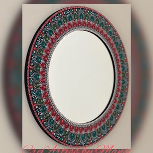 May include: A round mirror with a hand-painted mandala design in shades of red, green, and gray. The mirror is surrounded by a black frame.