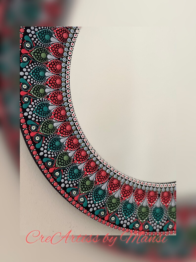 May include: A round mirror with a black frame decorated with a colorful mandala design. The mandala features red, green, and white dots arranged in a circular pattern.