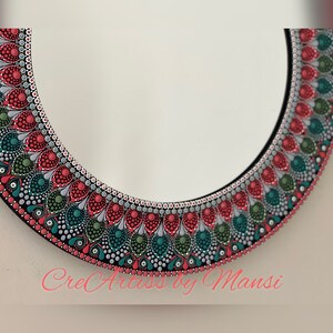May include: A round mirror with a decorative frame painted with red, green, and silver dots. The frame has a mandala-like design. The text "CreArts by Mansi" is visible at the bottom of the image.