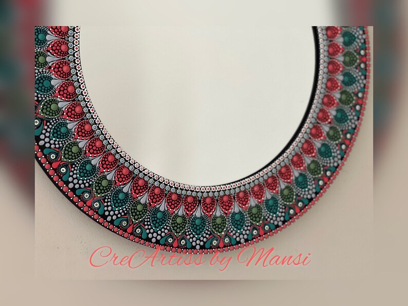 May include: A round mirror with a decorative frame painted with red, green, and silver dots. The frame has a mandala-like design. The text "CreArts by Mansi" is visible at the bottom of the image.
