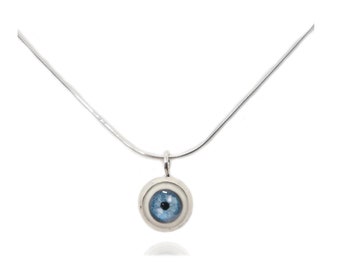 May include: A silver-toned necklace featuring a pendant with a detailed blue eye design. The eye has a light blue iris and a dark blue pupil, set within a circular, textured frame. The chain is a thin, snake-style design.