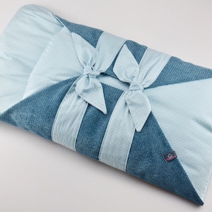 Pode incluir: Um envoltório para bebê azul e branco com um design de laço. O envoltório é feito de um tecido macio e texturizado.