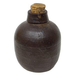 May include: A dark brown ceramic bottle with a cork stopper. The bottle has a rounded body and a slightly flared neck.