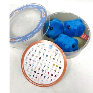May include: A round metal container with a clear plastic lid containing three bright blue plush toys shaped like microbes. The lid features the text GIANT microbes minis. A circular paper insert displays a collection of various microbe illustrations.