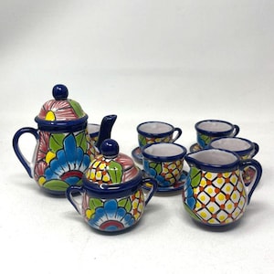 May include: A ceramic tea set featuring a teapot with a lid, a sugar bowl with a lid, a creamer, and four small cups with saucers. Each piece is hand-painted with vibrant blue, green, yellow, and red floral and geometric patterns on a white base.