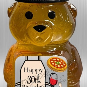 May include: A honey bear-shaped bottle with a black cap. The label reads "Happy 30th Birthday Sara!" and features illustrations of food items like pizza, sushi, a burger, and noodles. The bottle is filled with golden honey.