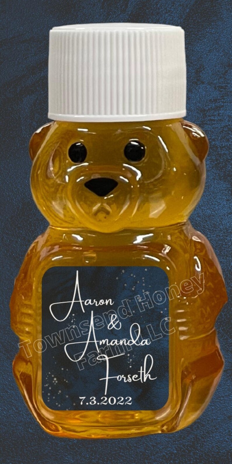 May include: A bear-shaped honey bottle with a white cap. The bottle has a label with the names "Aaron & Amanda Forseth" and the date "7.3.2022". The honey is a golden color.