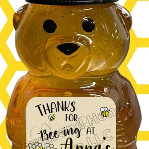 May include: A honey bear-shaped bottle filled with golden honey. The bottle has a black cap and a label that reads "Thanks for Bee-ing at Anna's Shower!" with bee and honeycomb graphics. The background features a yellow honeycomb pattern.