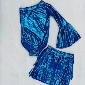 May include: A blue metallic one-shoulder bodysuit with long bell sleeves and a matching blue fringed skirt. The skirt has a high waist and is made of a shiny fabric.
