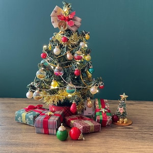 May include: A small Christmas tree adorned with baubles and fairy lights, topped with a bow. Several wrapped gift boxes and ornaments are arranged around the base of the tree, creating a festive holiday scene.