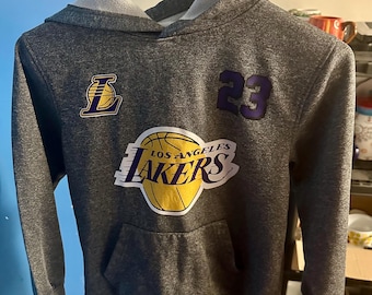 子供用Mサイズ、NBAロサンゼルス・レイカーズ、レブロン・ジェームズ #23 ヘザープルオーバーパーカー。胸にグラフィックロゴ入り。