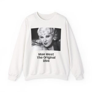 Può includere: Felpa bianca con un'immagine in bianco e nero di Mae West. L'immagine rettangolare include il testo "Mae West The Original Diva" in nero. La felpa ha un girocollo e maniche lunghe.