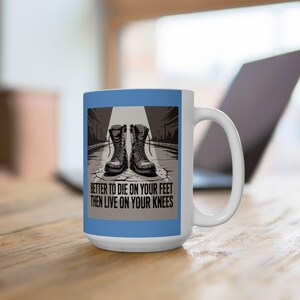 May include: White ceramic mug with a blue border featuring a graphic of combat boots on a cracked road. The text reads "BETTER TO DIE ON YOUR FEET THEN LIVE ON YOUR KNEES". The mug has a white handle.