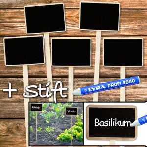 May include: Six small black chalkboard signs with white frames on wooden sticks. The signs are blank except for one that says "Basilikum". A blue and white marker is next to the sign. The signs are on a wooden background.