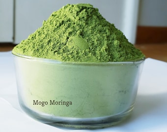 Op de afbeelding: Een glazen kom gevuld met een grote hoeveelheid felgroen moringa-poeder. Het etiket op de kom luidt "Mogo Moringa".