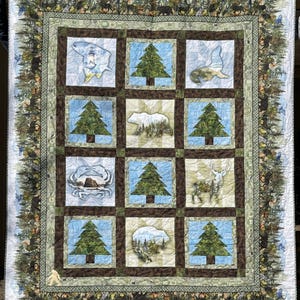 May include: A large, square quilt with a nature theme. The quilt features nine square panels with images of trees, animals, and landscapes. The border has a forest and mountain design. The color palette includes greens, blues, and browns.