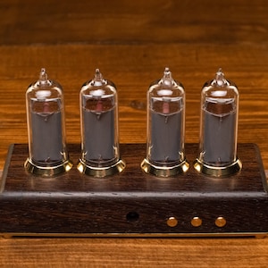 May include: Four clear glass Nixie tubes with black numerals on a dark wood base with gold accents. The tubes are lit and display the numbers 1, 2, 3, and 4.