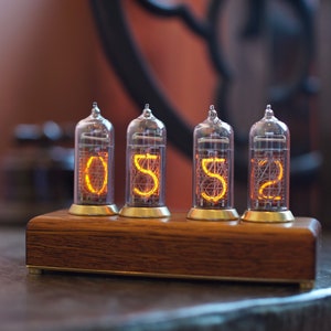 May include: A wooden clock with four clear glass tubes displaying the numbers 0552. The tubes are lit with a warm orange glow.