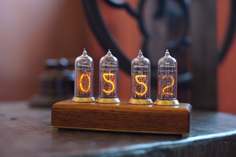 May include: A wooden clock with four clear glass tubes displaying the numbers 0552. The tubes are lit with a warm orange glow.