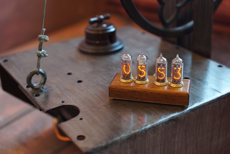 May include: A wooden base with four clear glass Nixie tubes displaying the numbers "0533". The tubes are lit with a warm orange glow.