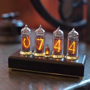 Puede incluir: Un reloj de estilo vintage con cuatro tubos Nixie que muestran la hora 07:44. El reloj est&aacute; hecho de madera oscura y tiene una base de lat&oacute;n.
