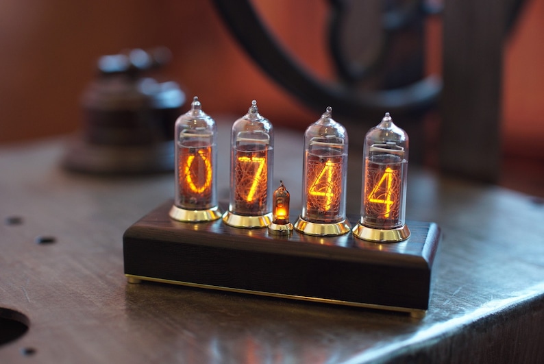 Puede incluir: Un reloj de estilo vintage con cuatro tubos Nixie que muestran la hora 07:44. El reloj est&aacute; hecho de madera oscura y tiene una base de lat&oacute;n.