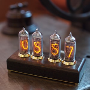 May include: A wooden clock with four Nixie tubes displaying the time 05:57. The tubes are lit with an orange glow and are set in a dark wood base.