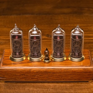 Puede incluir: Un reloj de madera con cuatro tubos Nixie de vidrio transparente que muestran la hora. El reloj est&aacute; sobre una superficie de madera.