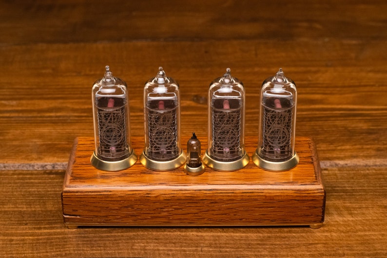 Puede incluir: Un reloj de madera con cuatro tubos Nixie de vidrio transparente que muestran la hora. El reloj est&aacute; sobre una superficie de madera.