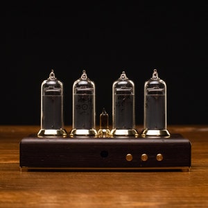 Puede incluir: Un reloj de estilo vintage con cuatro tubos Nixie de vidrio transparente que muestran la hora. El reloj est&aacute; montado sobre una base de madera oscura con detalles dorados.